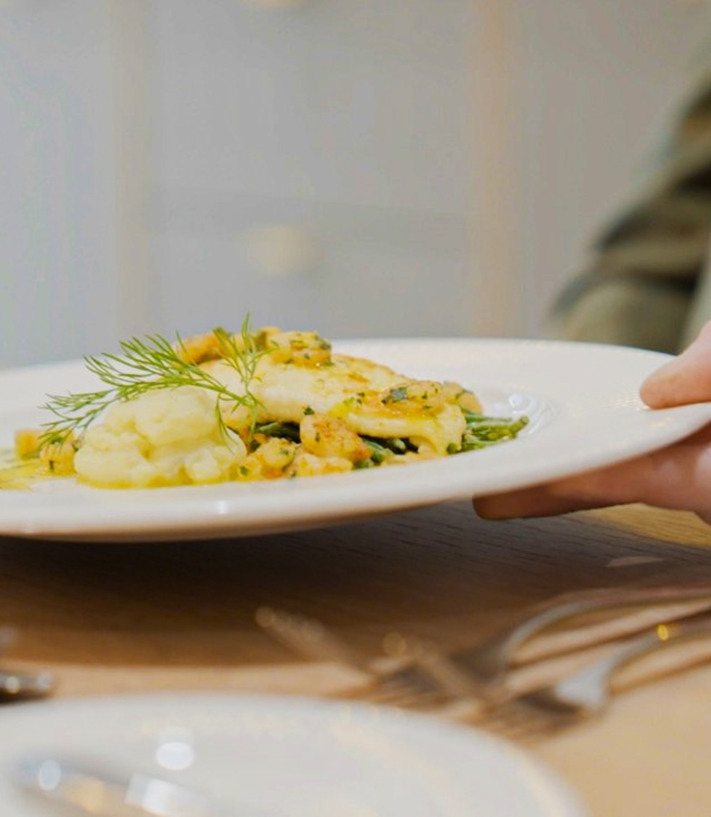A person holds a plate of food, showcasing a meal on a wooden table.